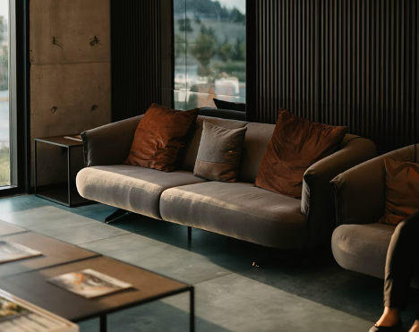Dark living room with dark walls, brown couch, during sunset coming through the window