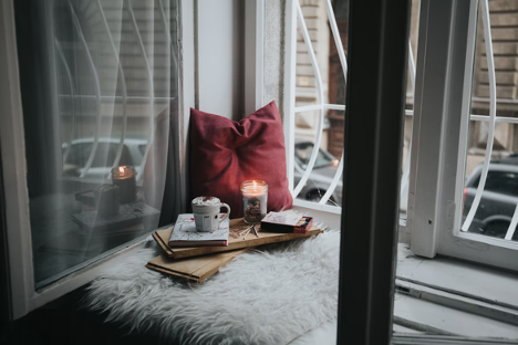 Cozy window ledge in a house with a pillows, tea, a candle, and books looking outside