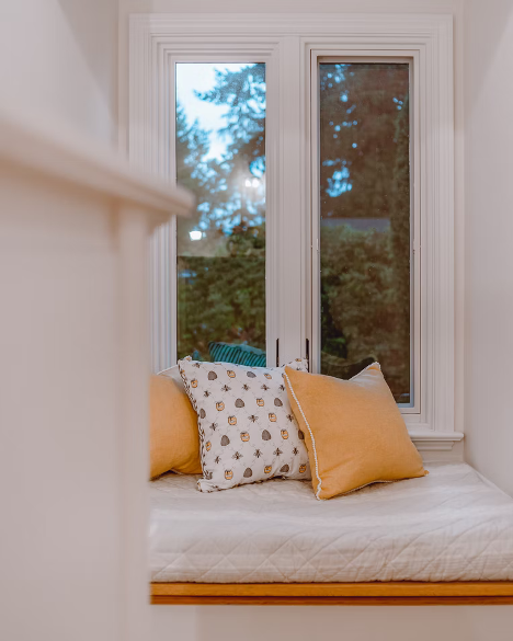 Small nook with a cushion and yellow pillows facing a window at dusk