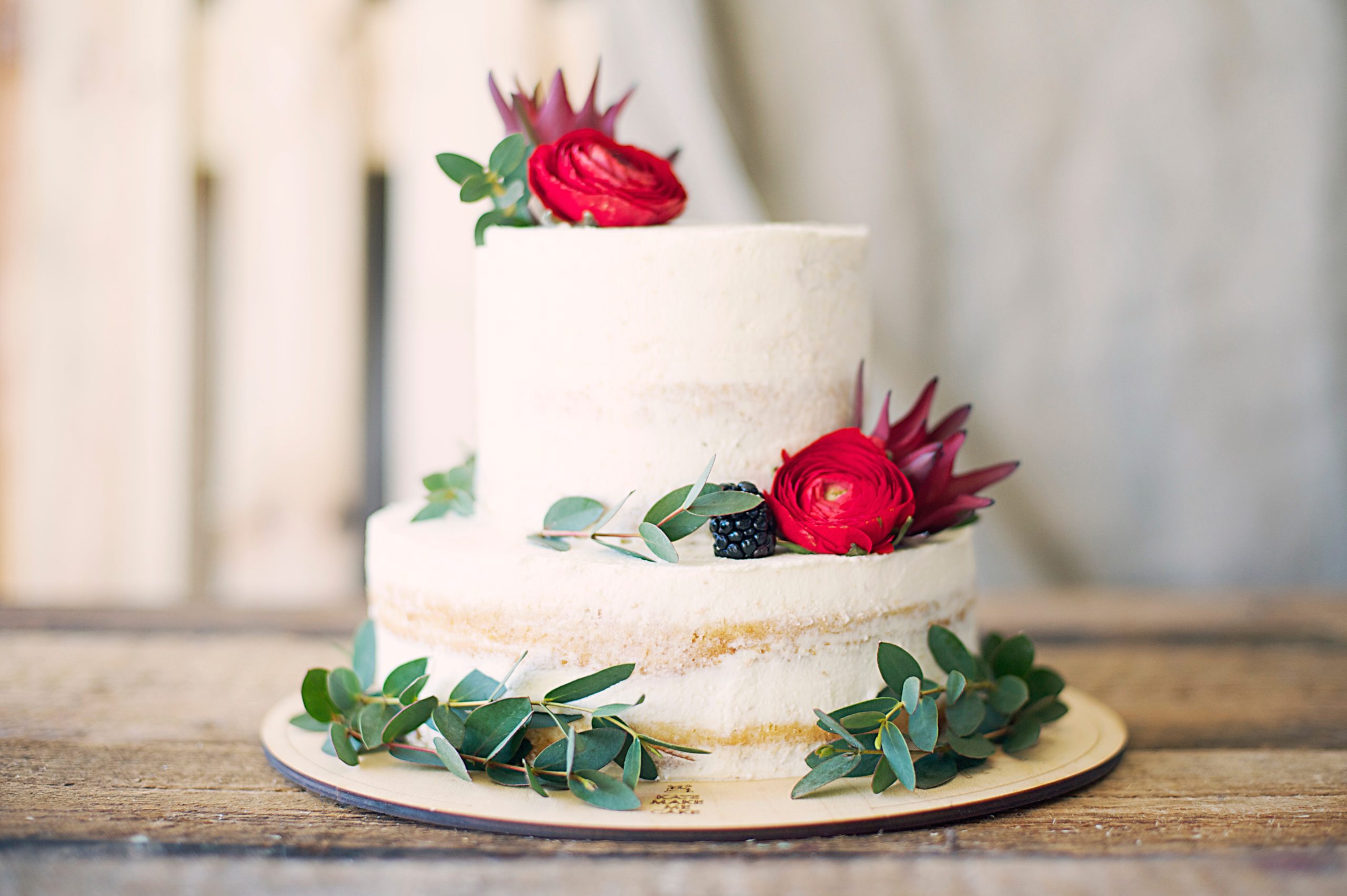 Decorated white cake with two tiers with roses, berries, and greenery along the outside