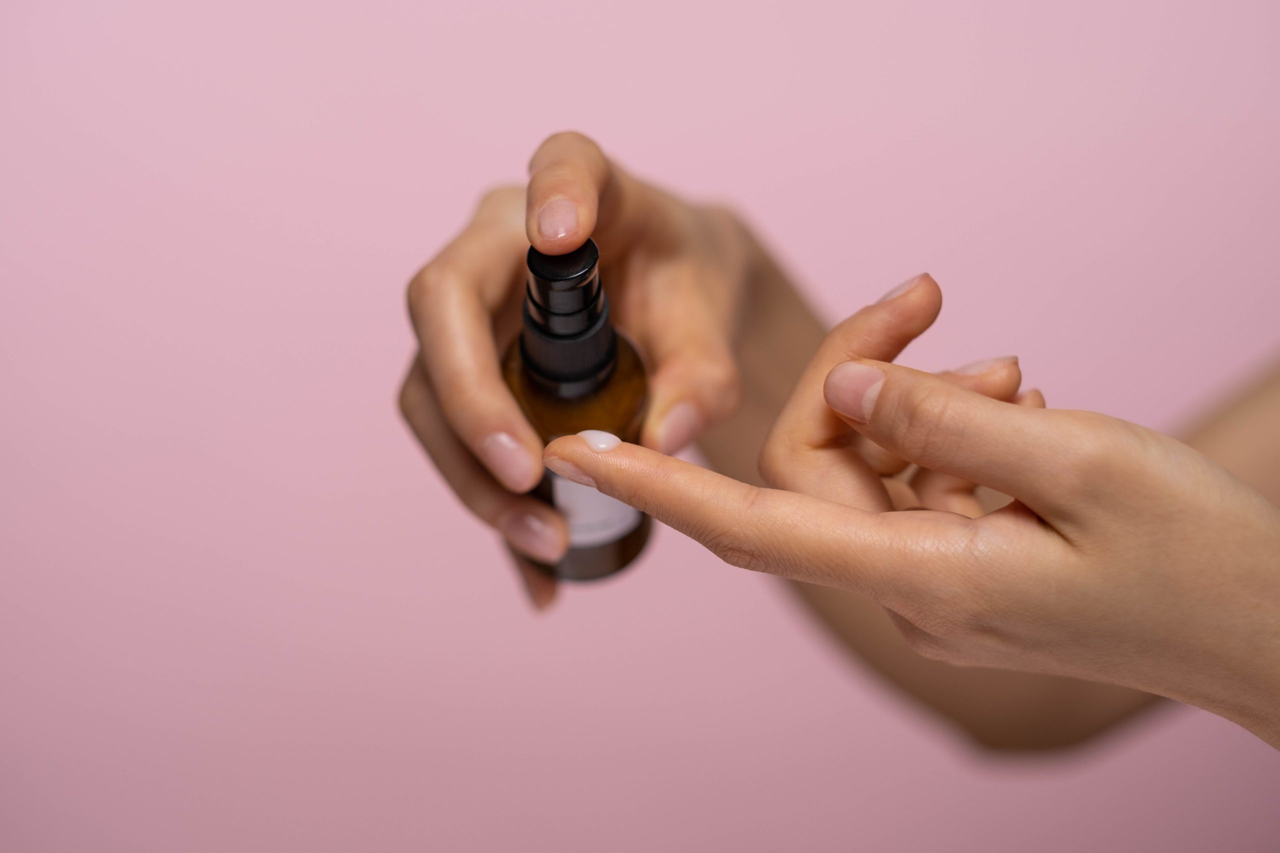 Woman pumping small bottle of lotion onto her finger in front of a pink background