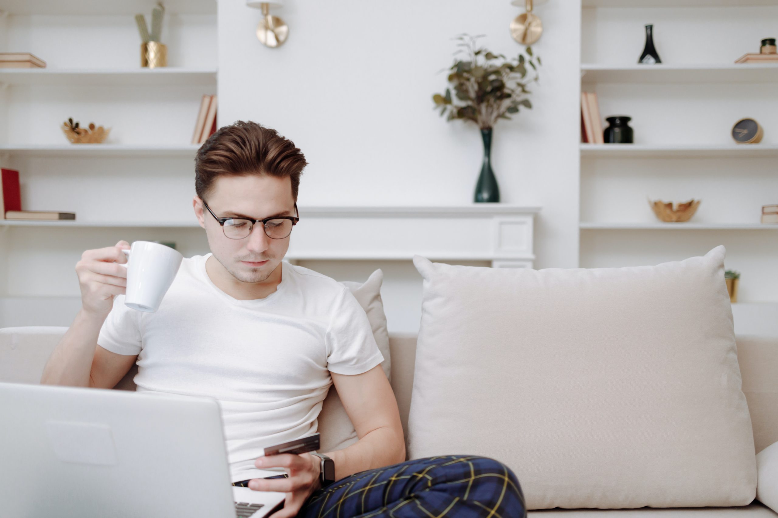 Man looking at credit card holding coffee in front of a laptop on the couch
