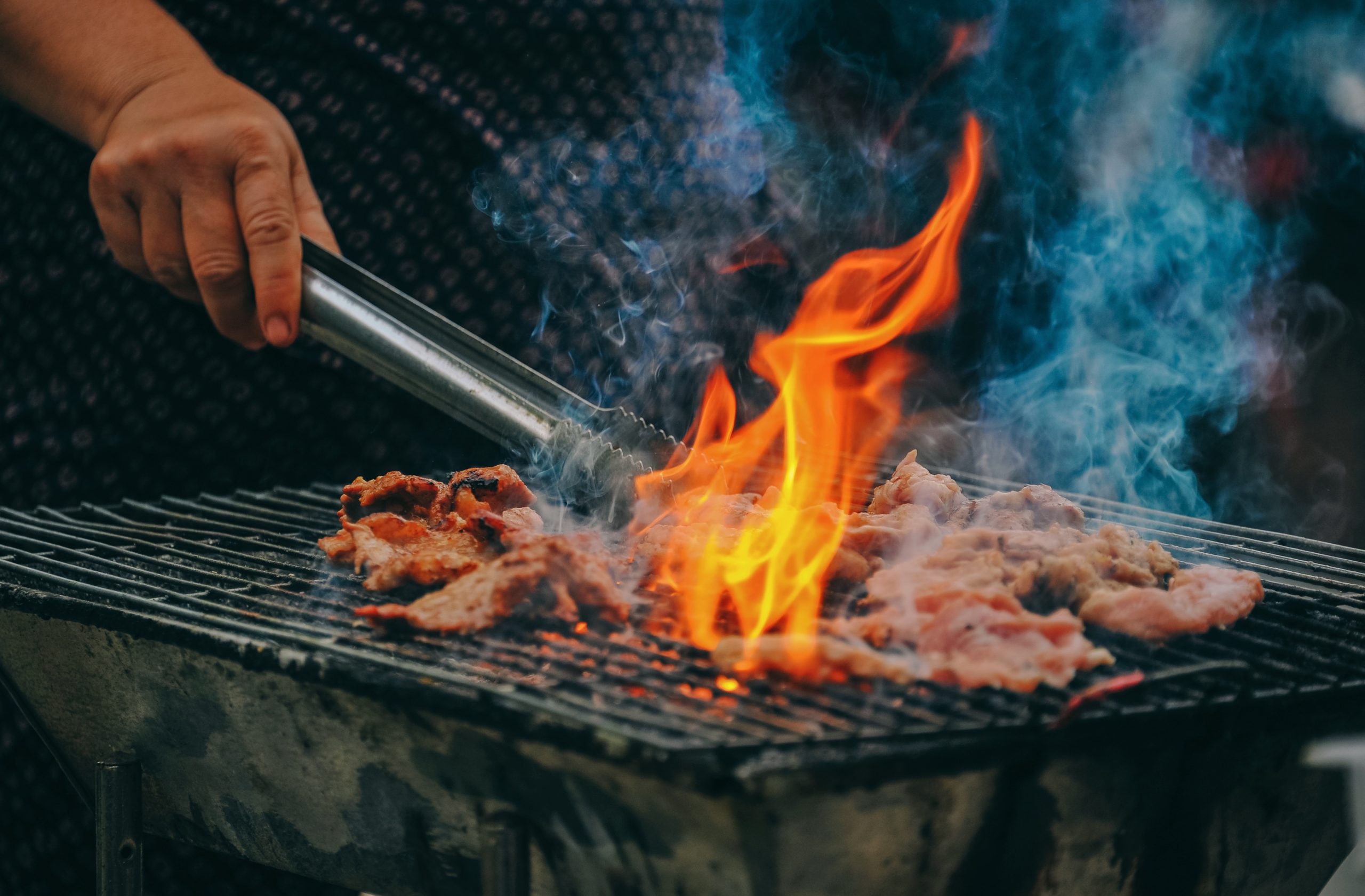Man grilling meat on an open fire grill with flames coming out