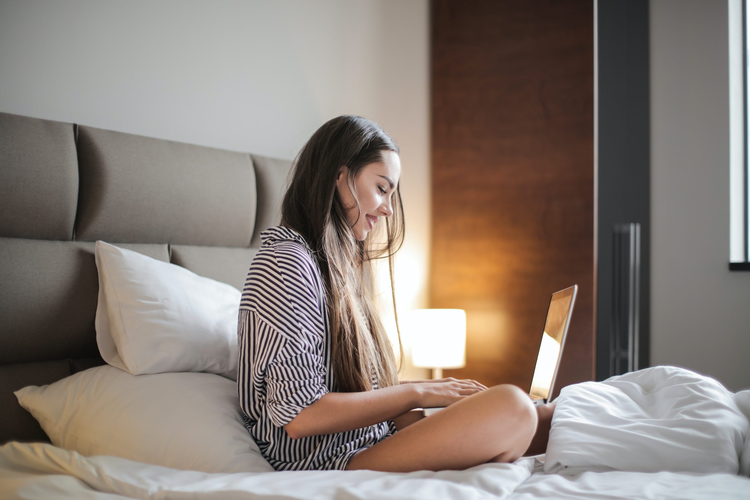 Woman sitting on a bed looking at a laptop