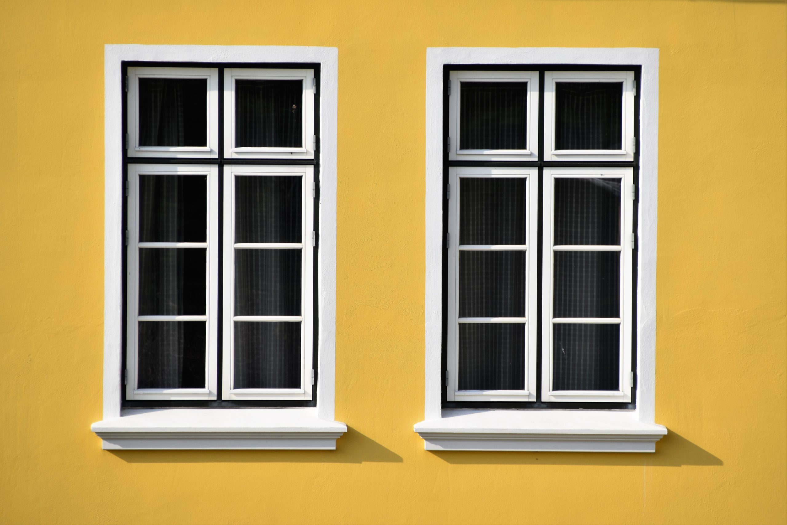 Set of two paned windows on a yellow wall with black curtains in behind