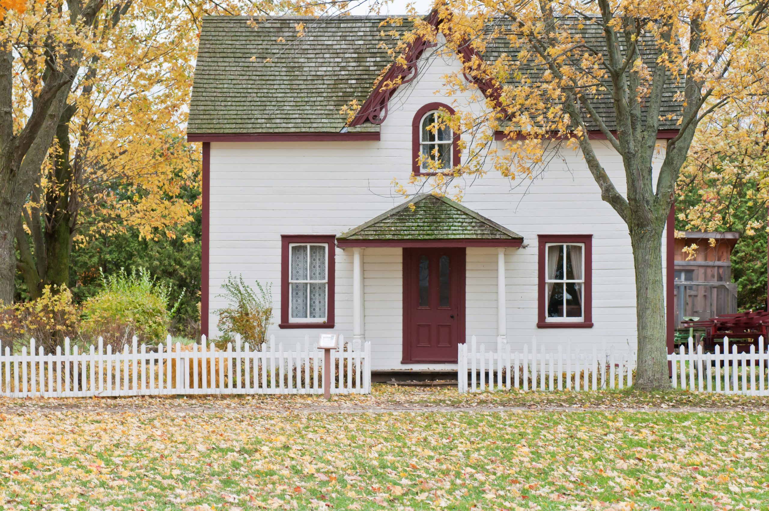 Exterior of a red and white house with many leaves on the ground during Fall