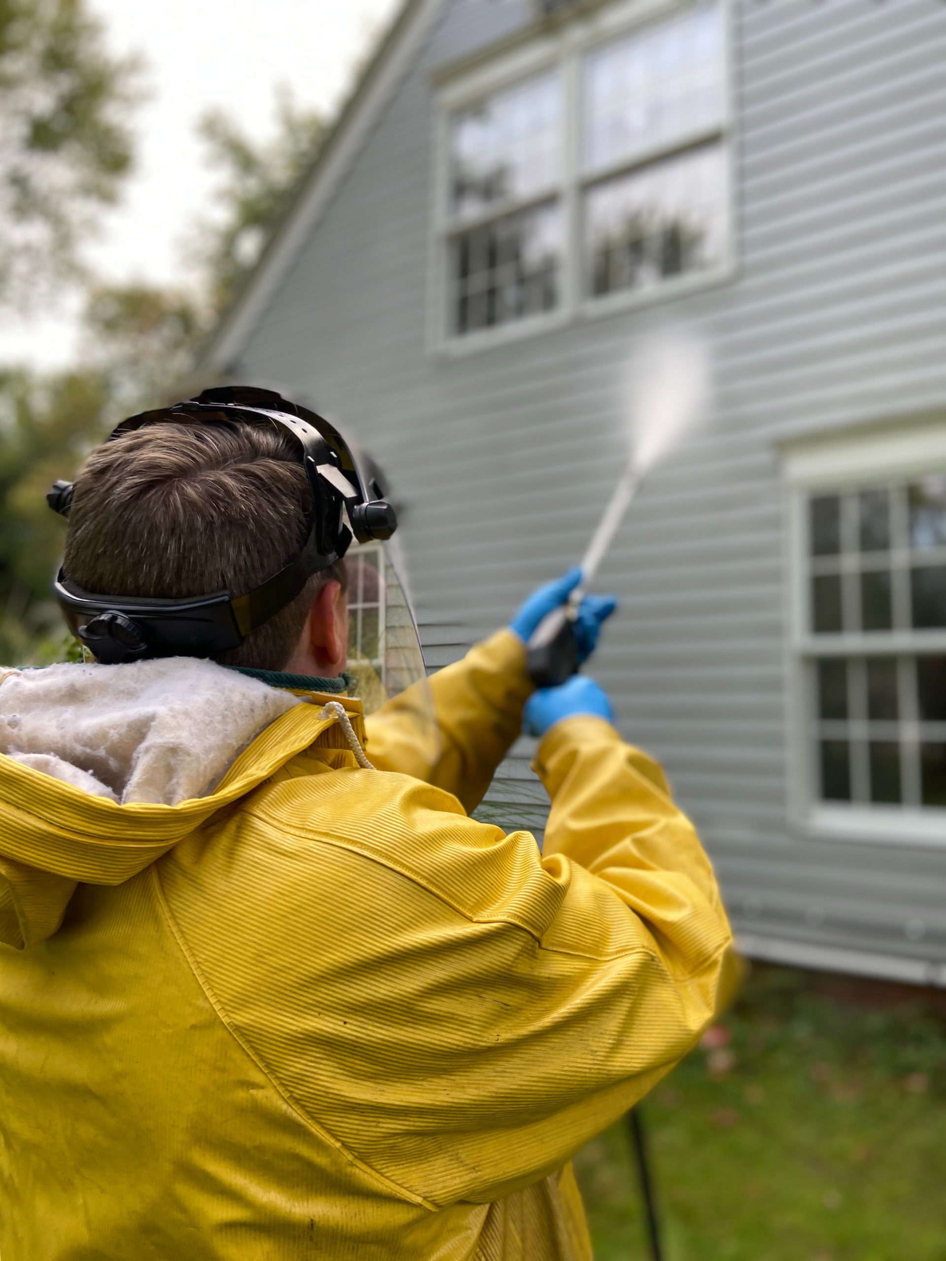 Man in yellow rain jacket pressure washing the exterior of a house