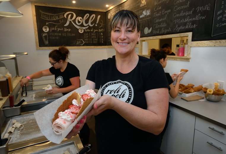 woman holding rolled ice cream taco in ice cream shop behind the counter