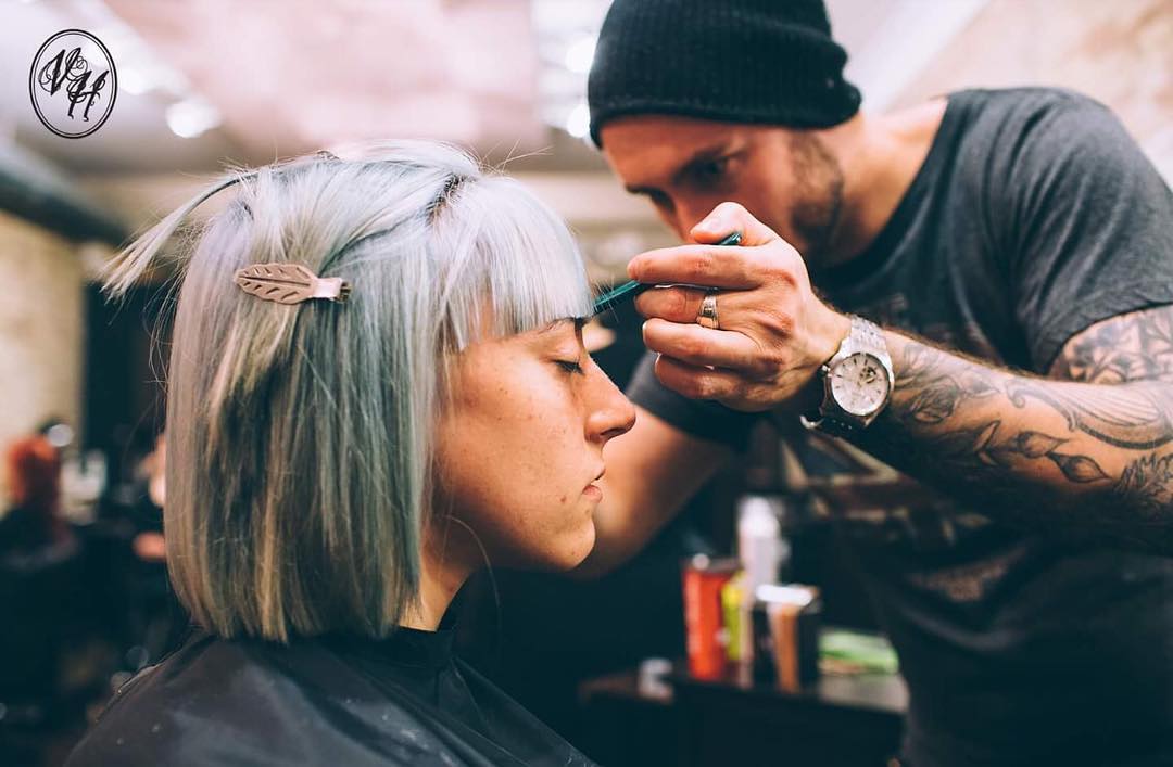 man with tattoos and watch cutting woman's hair