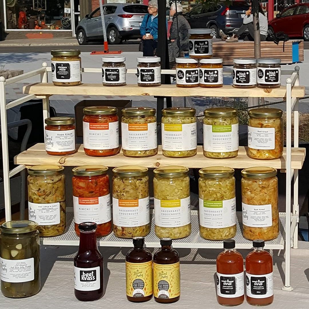variety of fermented items in jars at outdoor market on wooden shelf