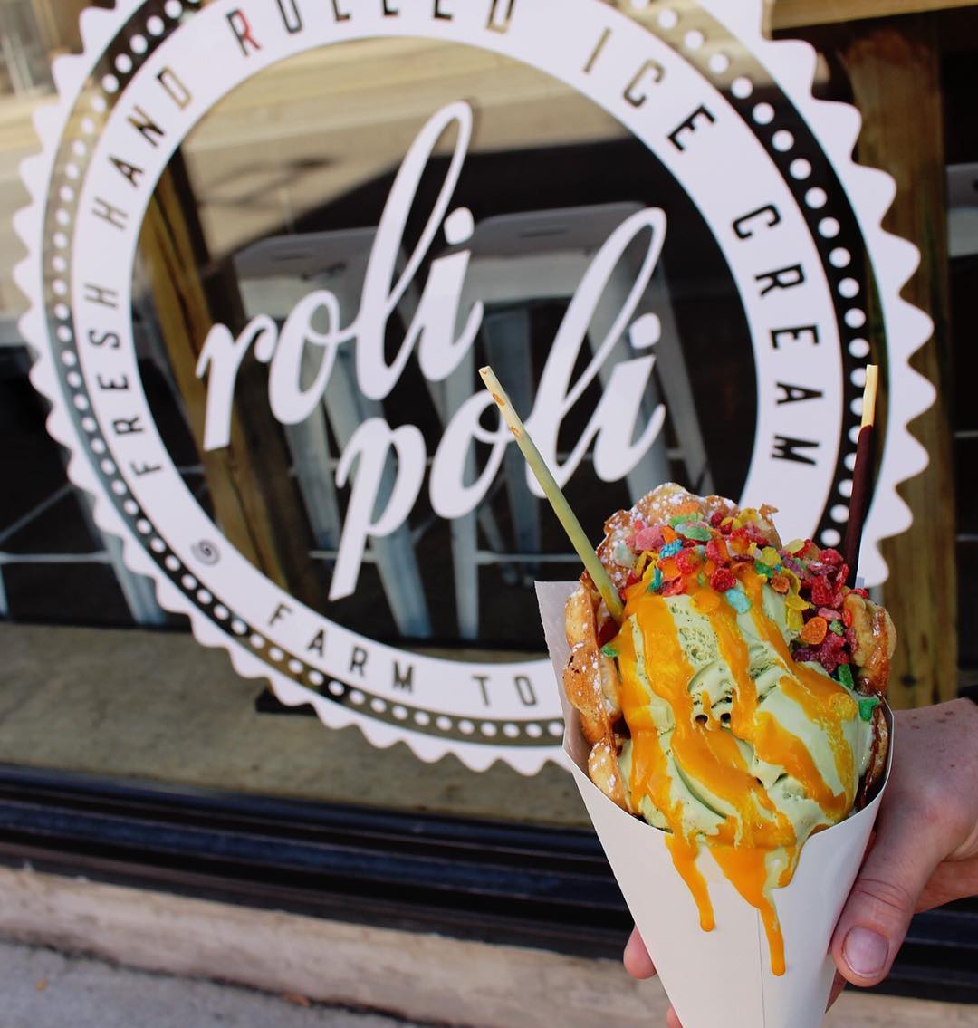 roli ice cream in cone held in front of parlour sign and logo in front of store
