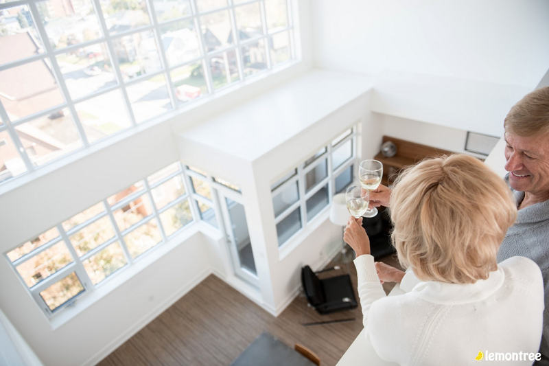 man and woman cheersing glasses overlooking inside of white home from second floor looking happy