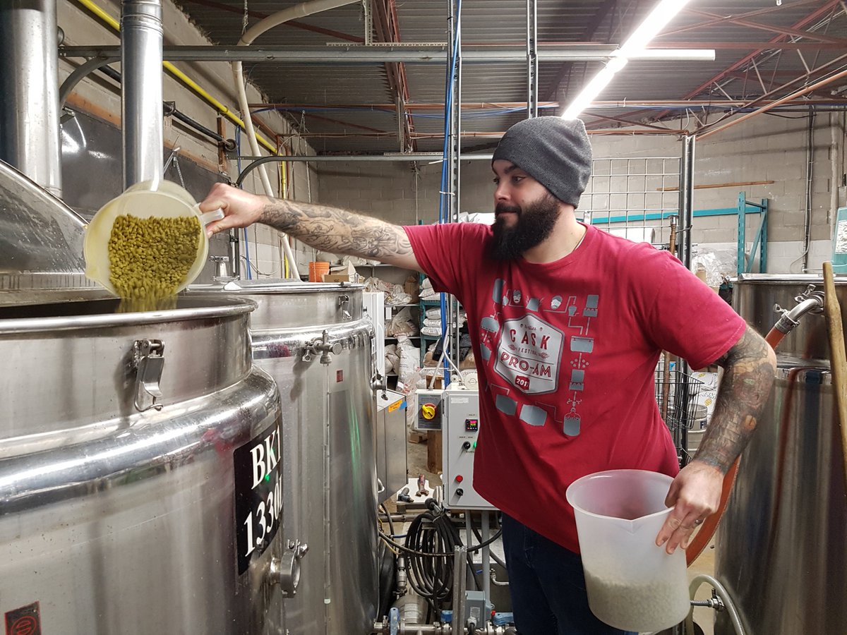 man pouring hops or barley inside large vat inside brewery to produce beer