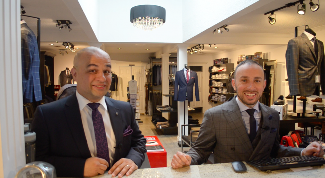 two mens formal clothing staff behind counter in front of store inventory