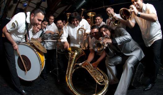 large band with various instruments posing as if playing and huddled toward downward camera