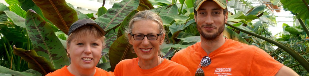 three gardening employees posing for photo inside greenhouse wearing orange