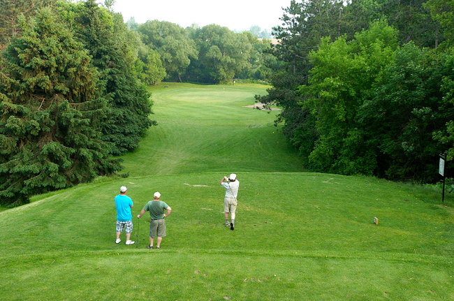 three golfers swinging off tee box at golf course with trees surrounding