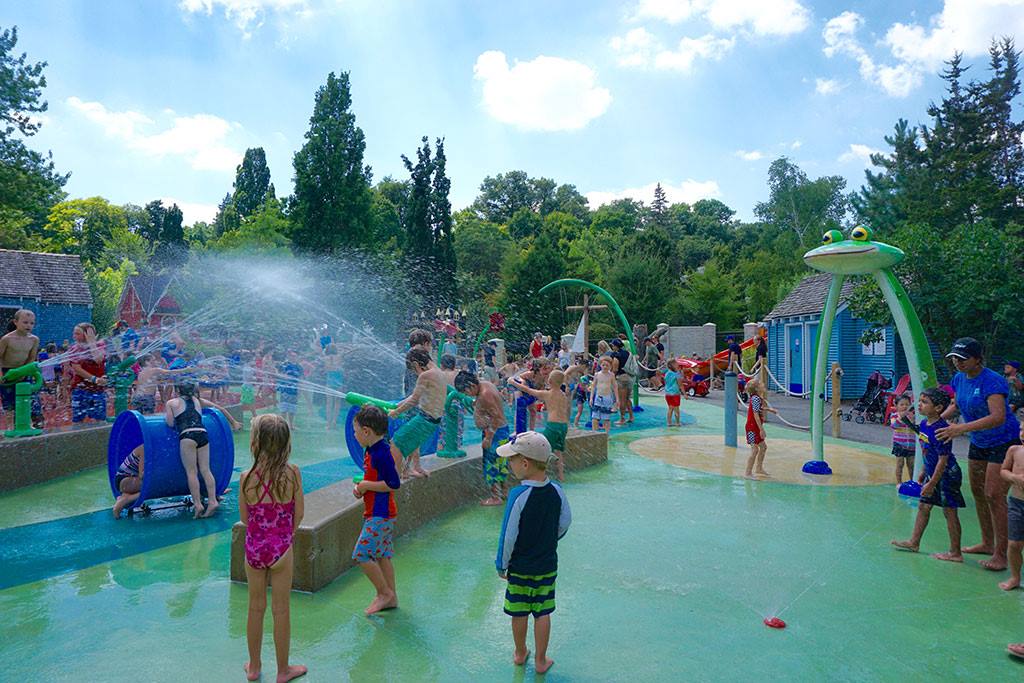 outdoor splash pad at kids park with many children and water spraying on a sunny day