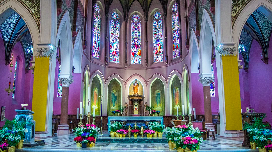 Cathedral interior with lots of flowers by the alter, stained glass and purple lighting throughout