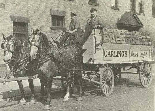 historic black and white photo of horse and buggy and two men with loaded cart behind