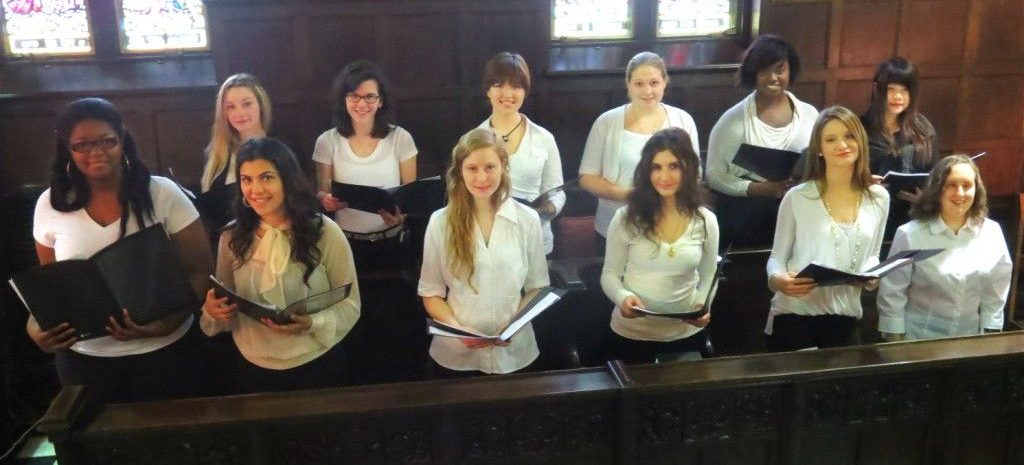 group of choir women holding books wearing white shirts behind a half wall