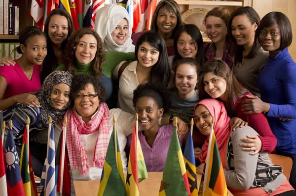 group of students in a room posing together for a photo in front of bookshelf and behind set of international flags