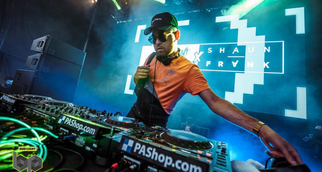 front shot of dj turning tables wearing sunglasses in front of large lit up screen