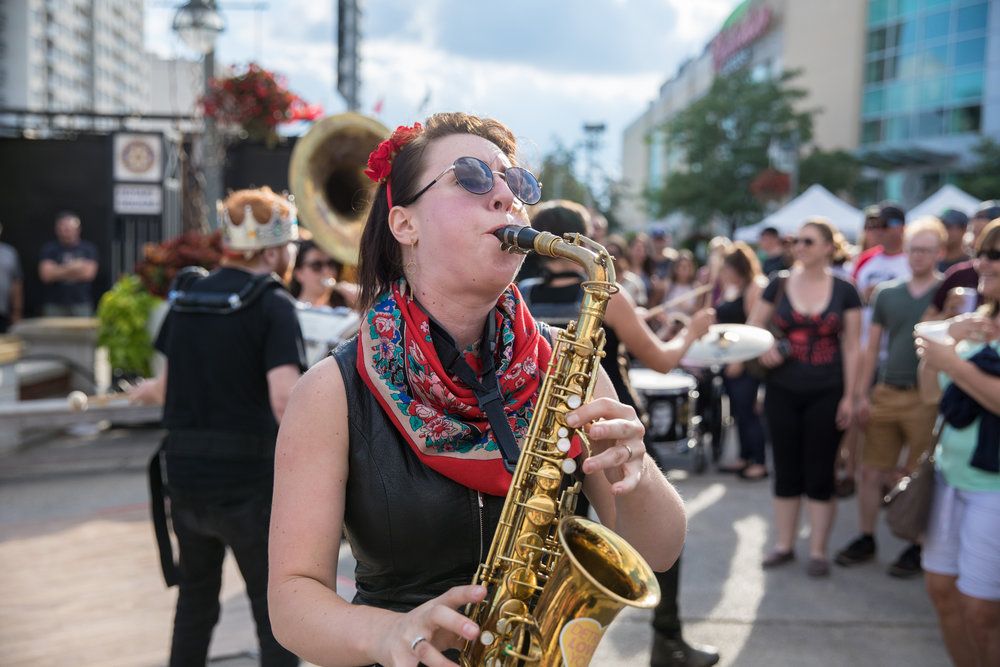 shot of woman playing saxophone wearing red accessories and sunglasses playing for outdoor street crowd