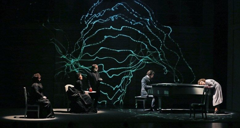 musical performance on stage with multiple people spaced out and man playing piano with green accents in background