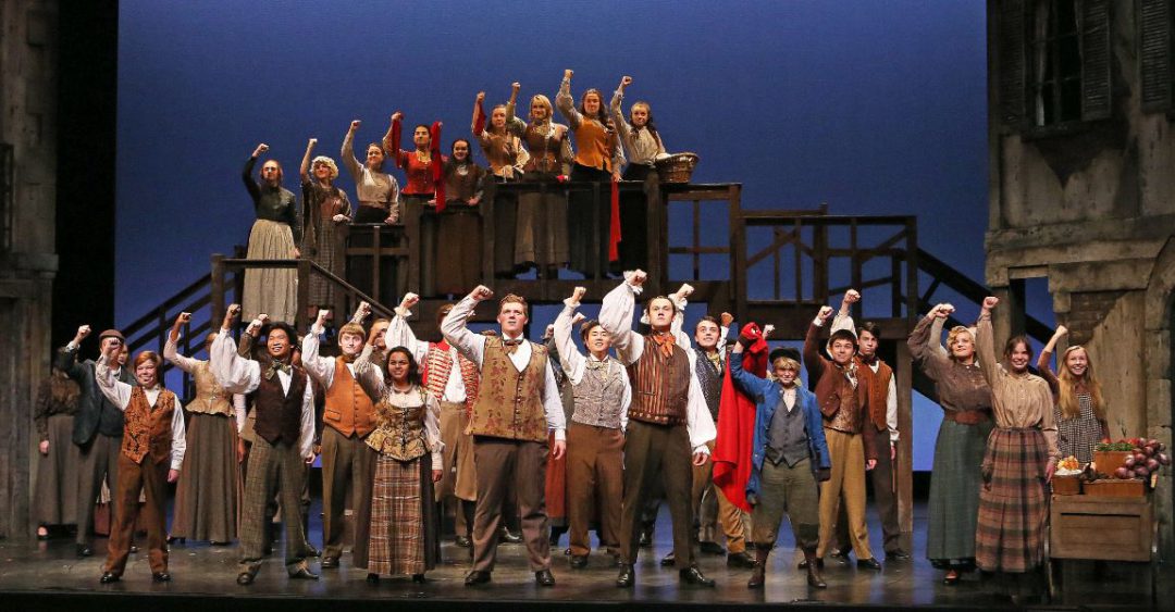 many actors in old costumes on stage raising fist