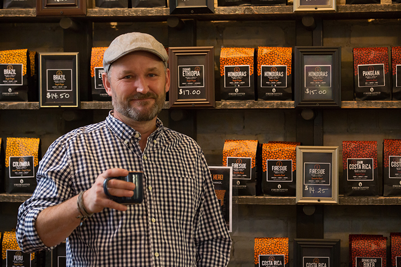 man standing holding up coffee mug in front of coffee bean packages