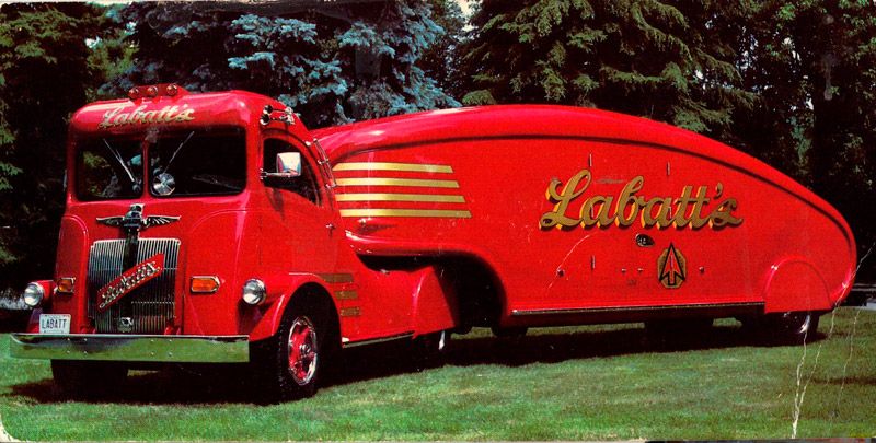 vintage red truck with large trailer with gold writing on the trailer in front of trees