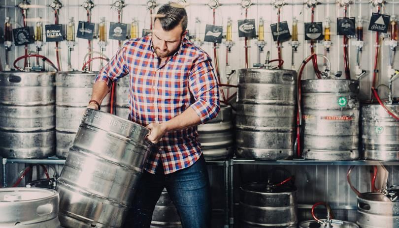 man moving a keg in room full of kegs with adjusters in background