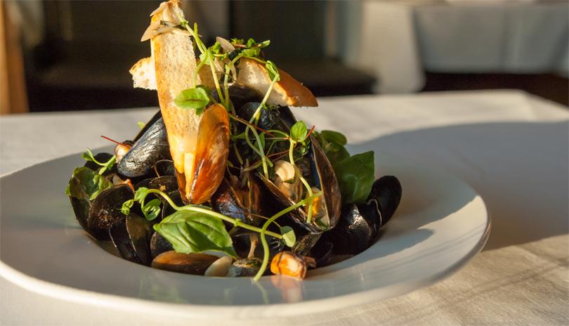 white bowl with mussels garnished with greens and two pieces of bread piled on top
