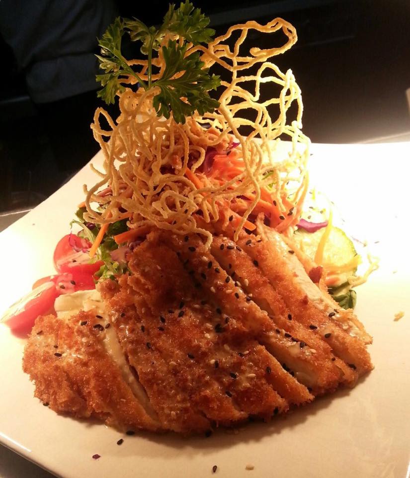 fried chicken on a white plate with fried noodle tower on top with green garnish
