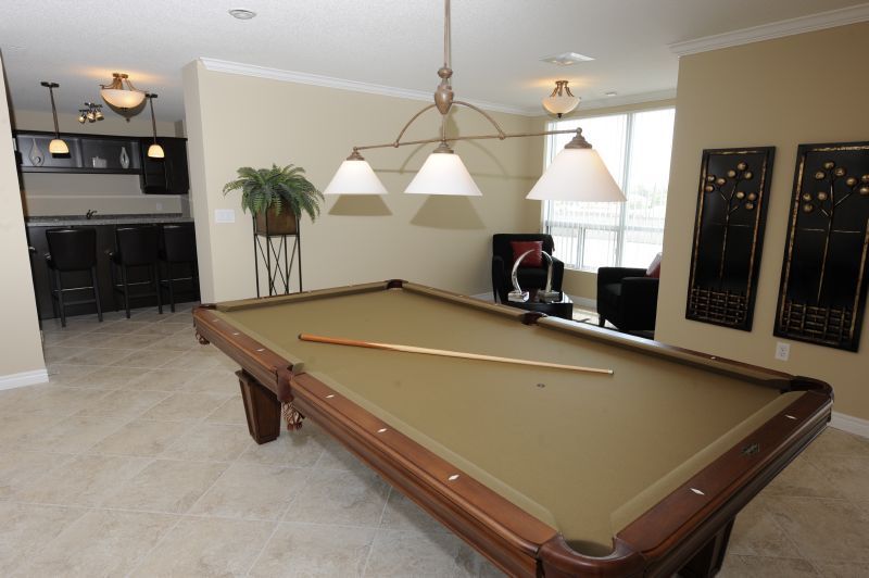 brown and beige pool table in front of two chairs in front of window and large black paintings