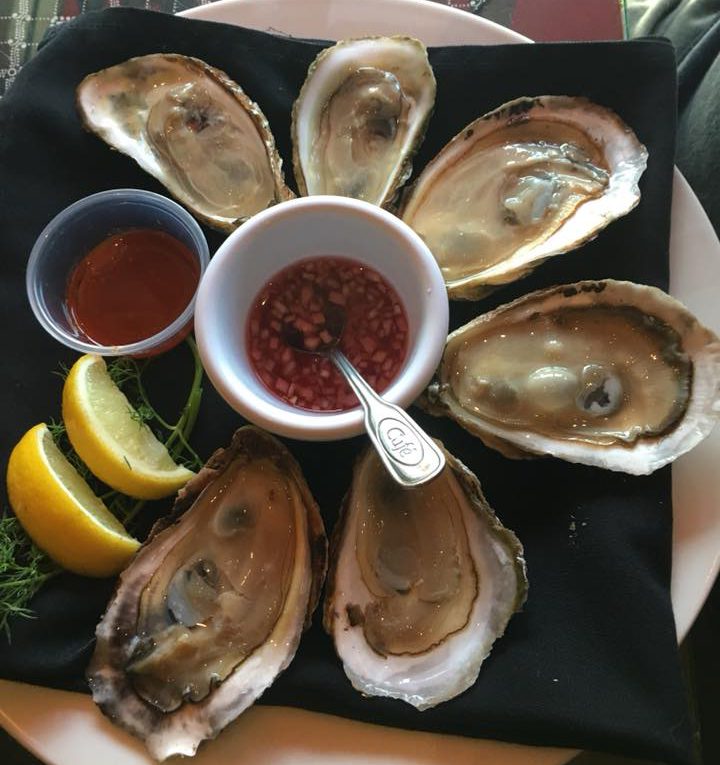 top view of oysters with sauce ramekins and lemon garnish on a black plate