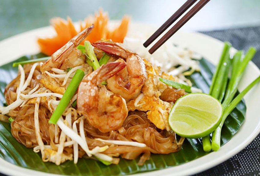 shrimp pad thai with lime on a plate with chop sticks