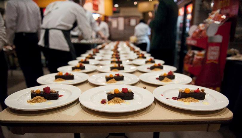 long row of plated desserts with chefs working in background