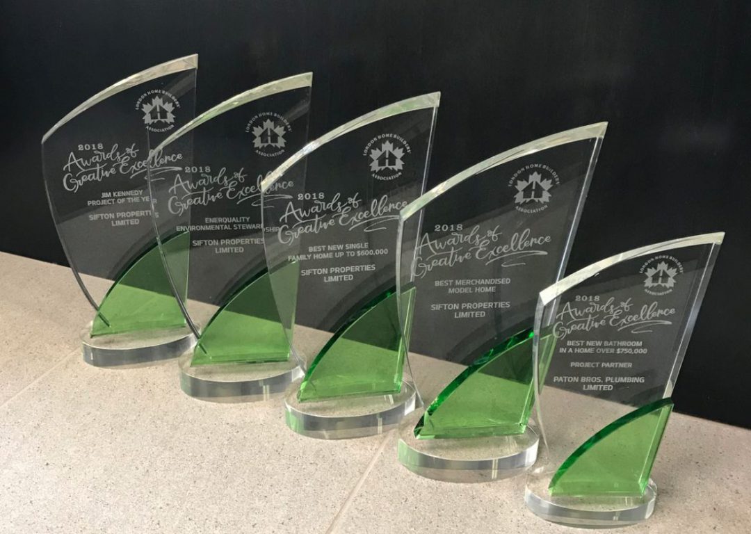 five glass trophies lined up on table with green accents on each