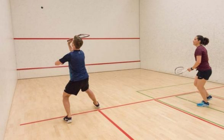 couple playing squash in court with ball in the air