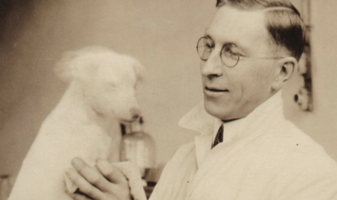 man in white lab coat and glasses holding dog and smiling
