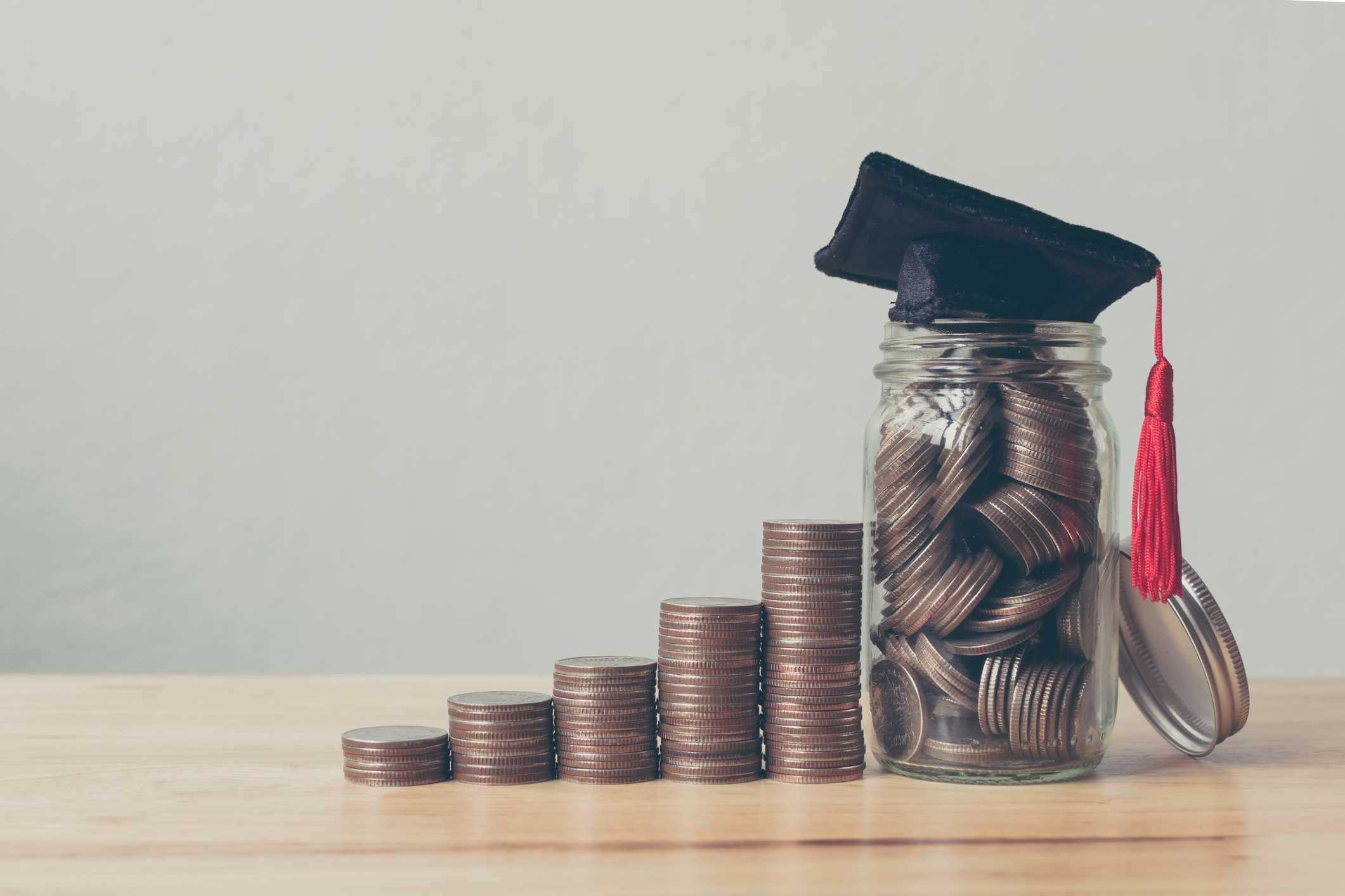 stacks of coins in ascending growth with jar as last stack with graduation cap on top