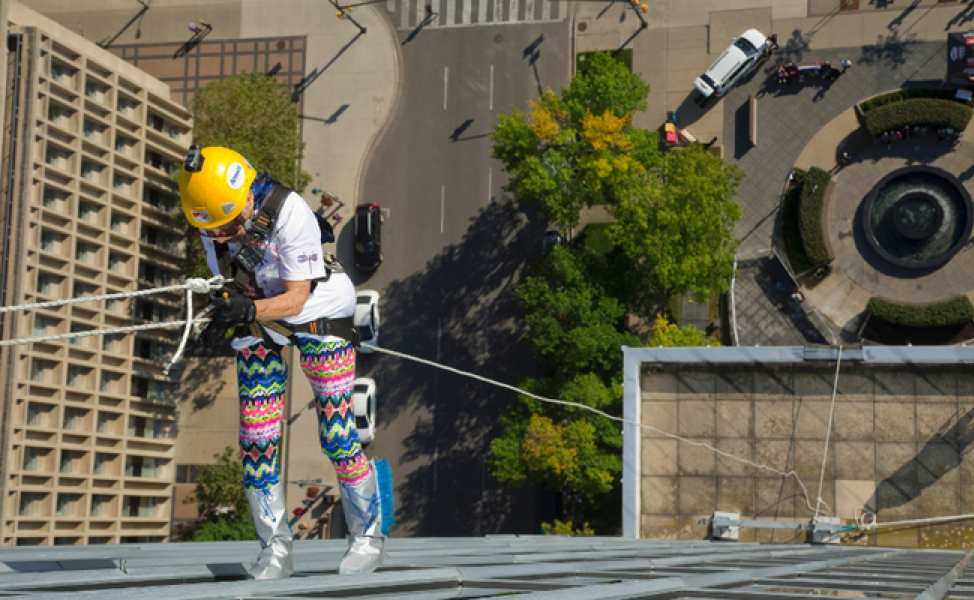 women rappelling down large building wearing a yellow helmet with cars below