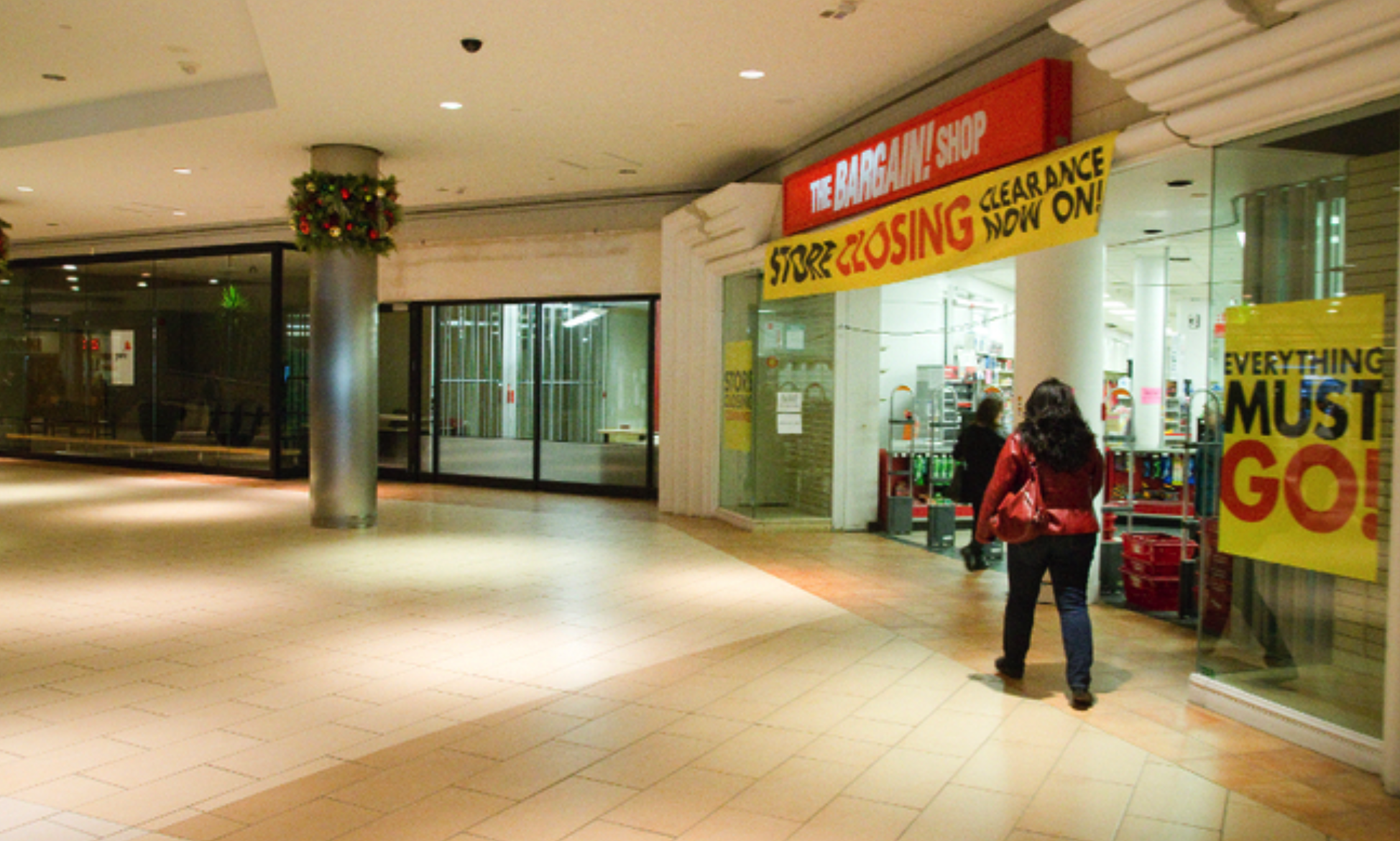 woman walking through mall with many closed stores and closing store sign above