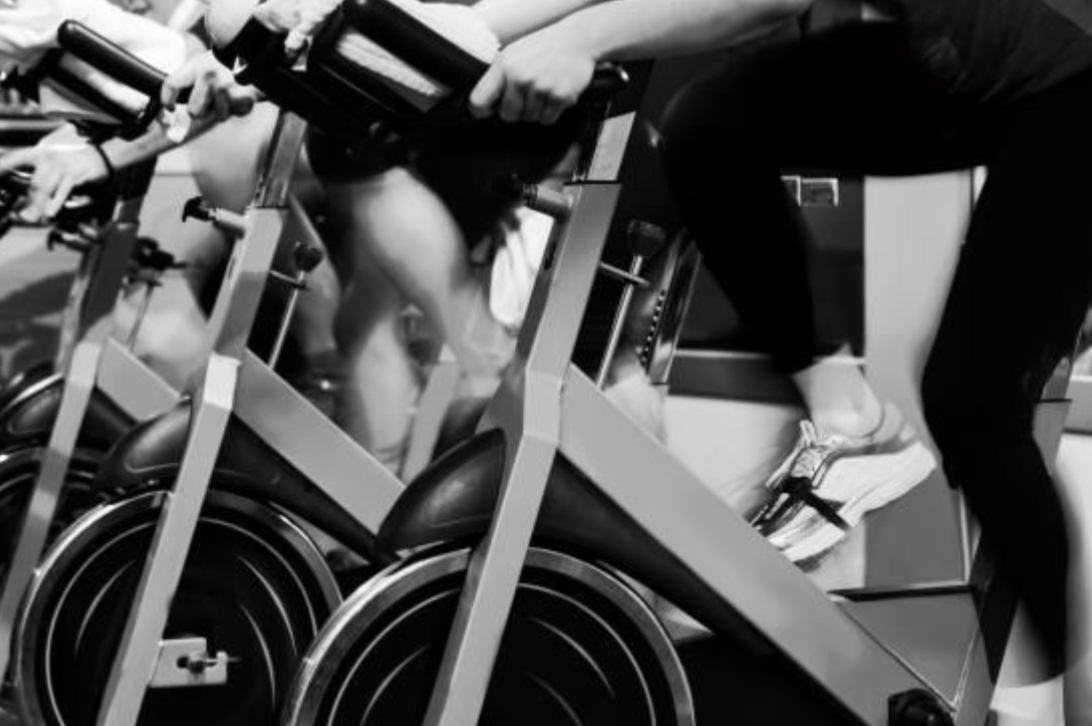 stationary bikes in black and white with people riding them only lower half showing