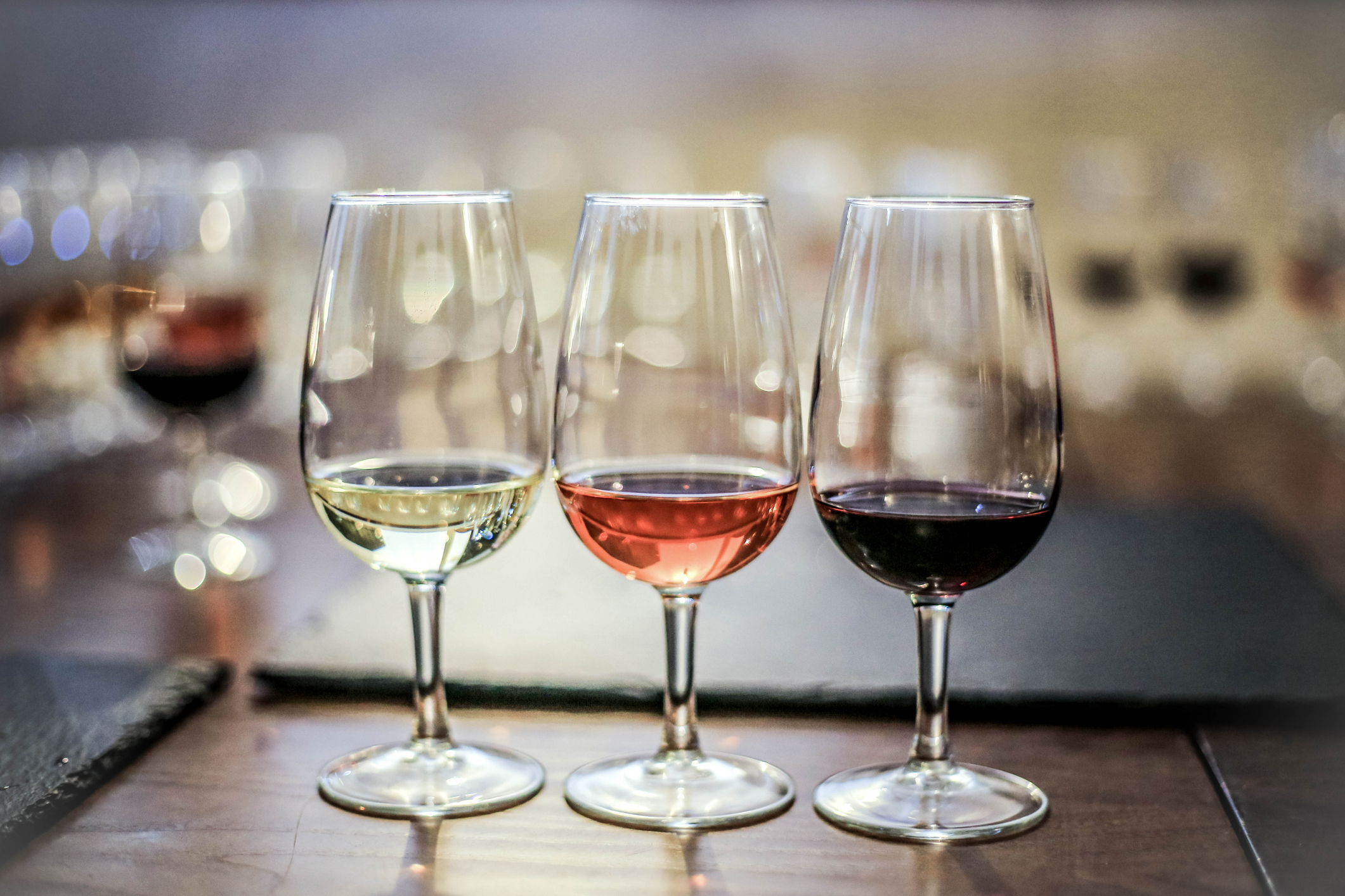 3 wine glasses with different coloured wine on a wooden table